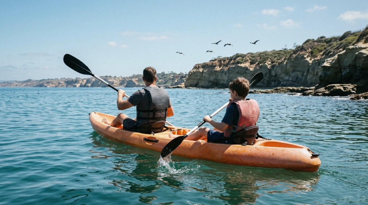 A parent and child in a tandem kayak paddling toward the La Jolla sea caves on a family kayaking trip in La Jolla, California